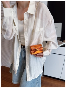 Detail view of mini metallic orange crossbody bag with oversized bow and gold chain strap
