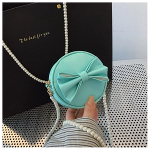 Détail du mini sac rond vert menthe avec un nœud et une bandoulière en perles blanches