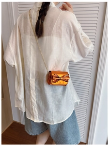 Detailed view of mini metallic orange patent leather bag with bow and gold chain strap