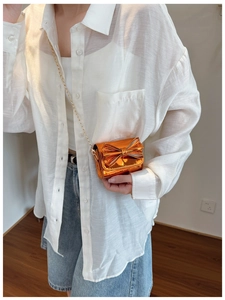 Detail of mini orange metallic bow bag with mirror finish and gold chain strap