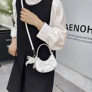 White crescent mini handbag with pearl bow charm shown in a minimalist modern setting