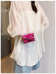 Detail of pink mirror mini bag with large bow and gold chain strap on a model