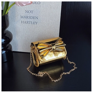 Detail of a gold metallic mirror mini bag featuring a large bow and gold chain strap