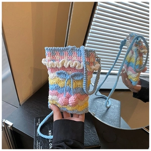Detail of handmade rainbow crochet bag featuring a blue bow and pink yarn pom-poms