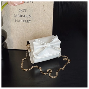Detail of a white patent leather mini bag with a bow and gold chain strap on a table