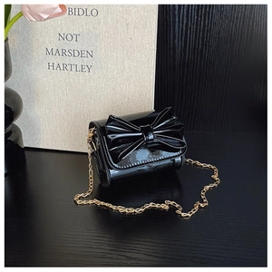 Close-up of black patent leather mini bag featuring a large bow and gold chain strap