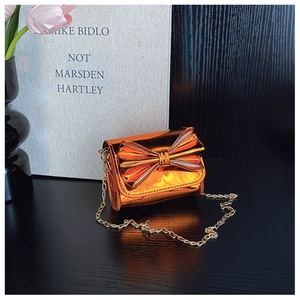 Detail of a mini metallic orange crossbody bag with a large bow and gold chain strap