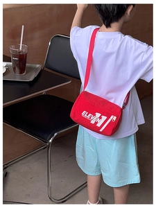 Borsa a tracolla rossa in nylon per bambini con scritte bianche indossata da un bimbo