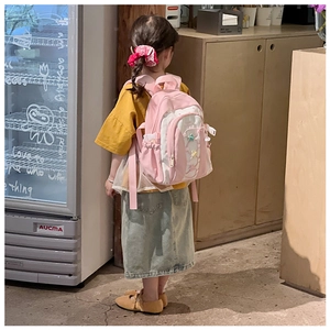 Pink cartoon kids backpack with star charms shown on model in a cozy indoor setting