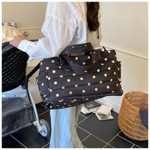 Quilted black tote bag with gold polka dots and shoulder strap shown in a lifestyle setting