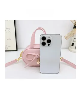 Pink mini crossbody bag with bow detail and gold heart charm shown next to a smartphone