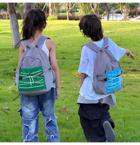 Rear view of children wearing high-capacity contrast color backpacks on a grassy field