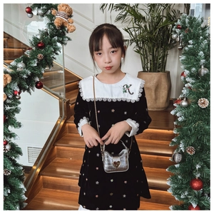 Close-up of heart-shaped silver accessory on black velvet girls dress with floral embroidery