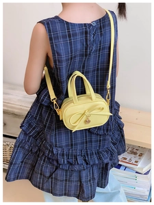 Detail of yellow kids' handbag featuring a large bow and golden heart charm on strap