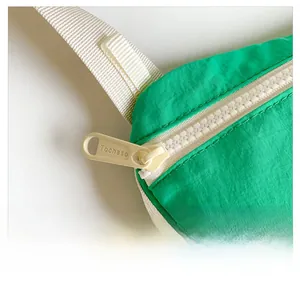 Nahaufnahme des glatten weißen Reißverschlusses an der grünen Kinderbauchtasche aus Nylon