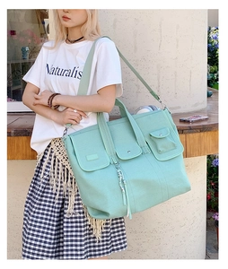 Outdoor view of a large mint green canvas tote bag with triple front pockets and wide strap