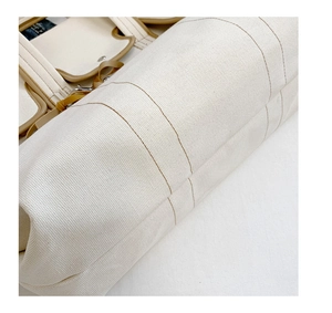 Detail of reinforced canvas texture and premium brown leather trim on a white tote bag