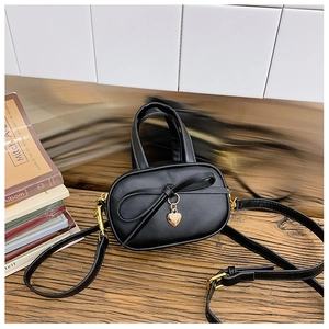 Detail of mini black faux leather handbag with sweet bow and golden heart pendant