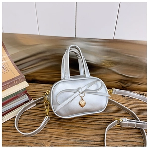 Detail of silver mini bag with a leather bow and golden heart pendant on wooden table