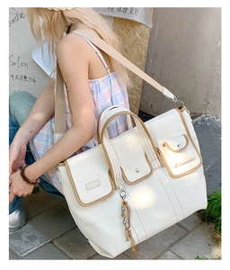 Detailed side view of a white canvas tote bag with brown trim and multi-pocket design