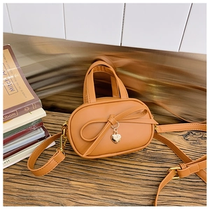 Close-up of tan mini handbag featuring a leather bow and a gold heart pendant detail