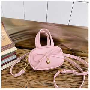 Detailed macro view of pink mini handbag with bow decoration and heart charm on wood surface