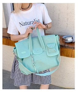 Detail of mint green canvas tote bag featuring three front pockets and crossbody strap