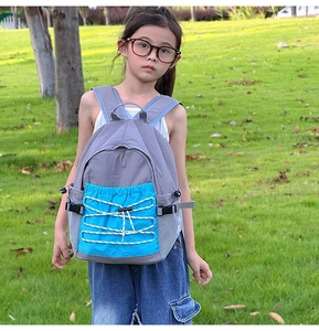 Detailed view of child wearing blue and grey outdoor backpack on a natural grass background