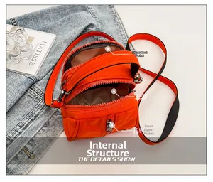 Detail of orange mini crossbody bag with three zipper pockets on denim background