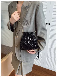 Detail of black sequined drawstring bucket bag with gold metal chain strap on model