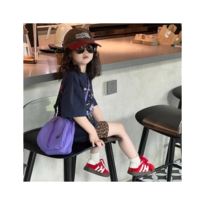 A small purple nylon crossbody bag for kids styled in a modern cafe setting