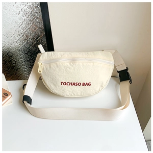 Detail der beige Nylontasche mit rotem Schriftzug und verstellbarem schwarzem Gurt