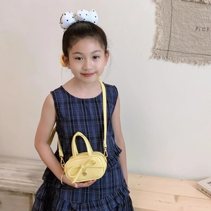 Mini yellow shoulder bag with bow and heart pendant shown on a young girl in a room