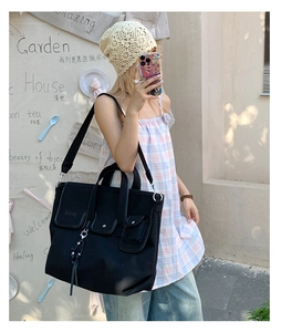 Detail of black canvas tote bag showing three front flap pockets with metal buckles