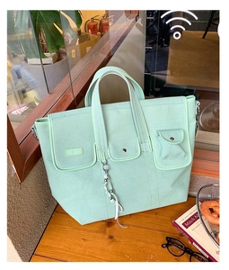 Detail view of a mint green canvas tote bag with functional multi-pockets on a wooden table