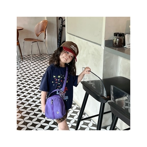 Close-up of a child wearing a purple nylon crossbody bag in a cozy cafe setting