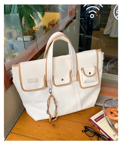 Detail of white canvas tote bag with brown trim and multiple functional front pockets
