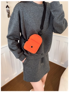 Close-up of a bright orange mini crossbody bag with adjustable strap worn on casual outfit
