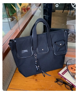 Detail of black canvas tote bag with multi-pocket design and leather trim on wooden table