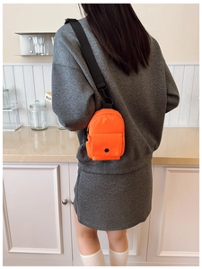 Close-up of bright orange mini chest bag worn over a gray sweatshirt in a home setting