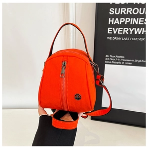Detail of bright orange nylon kids shell bag with metal M logo and adjustable strap