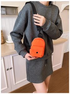 Detail of vibrant orange mini crossbody chest bag featuring adjustable black strap and pockets