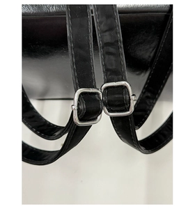 Macro detail of adjustable shoulder strap with silver buckle on black leather backpack