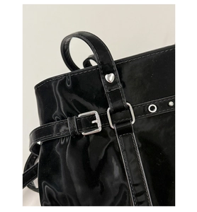 Close-up of black glossy patent leather bag with heart rivets and silver buckles