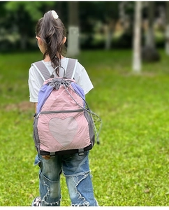 Pink and purple heart drawstring backpack shown on a child in an outdoor park setting