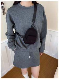 Close-up of black nylon mini crossbody bag with metal hooks on casual grey outfit