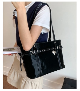 Detail of black patent leather tote bag with silver heart charm on model