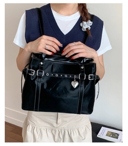 Close-up of glossy black bucket bag with silver buckles and a heart-shaped pendant
