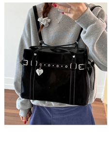 Detail of black patent leather tote bag featuring silver heart charm and metal buckles