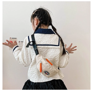 Detail of cream canvas kids chest bag with orange zipper pull and sport patch